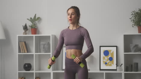young-pretty-woman-is-doing-exercises-with-dumbbells-in-apartment-sporty-woman-is-training-in-interior-of-modern-flat-medium-portrait-of-sportswoman